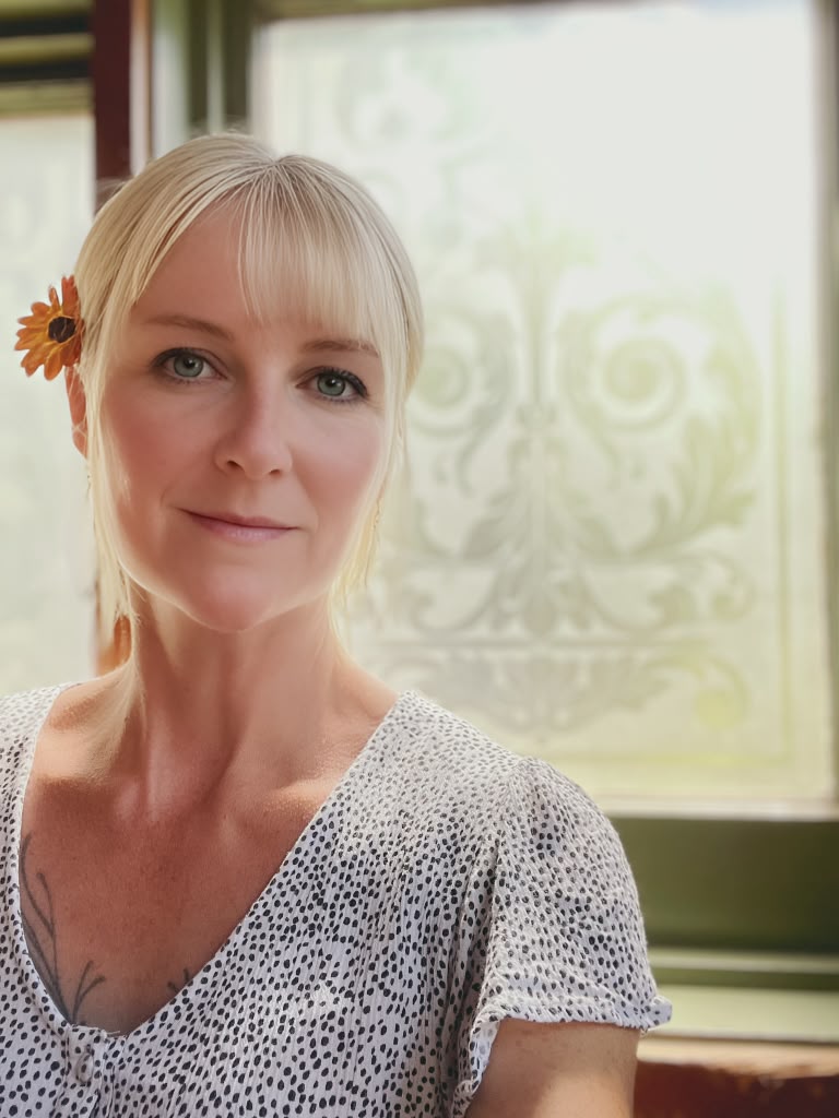 Portrait of Julia Harriet, smiling in front of a soft patterned window